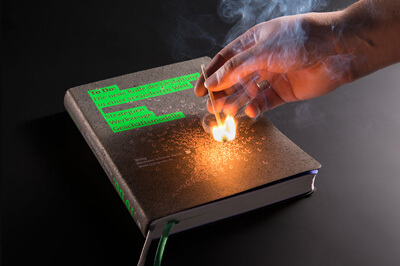 Ein Buch auf dem eine Veredelung mit Streichholz-Reibefläche ist und eine Hand die das Streichholz damit anzündet