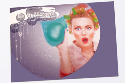 Eine blonde Frau mit Lockenwicklern, aufgerissenen Augen und aufgerissenem rot geschminkten Mund putzt mit einem blauem Tuch und darunter steht "Alles sauber!"