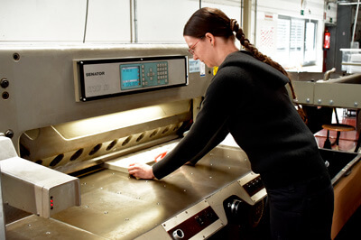 Frau die Druckbogen an der Schneidemaschine schneidet